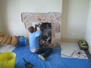 a stove installer breaking out a fireplace with a hammer drill