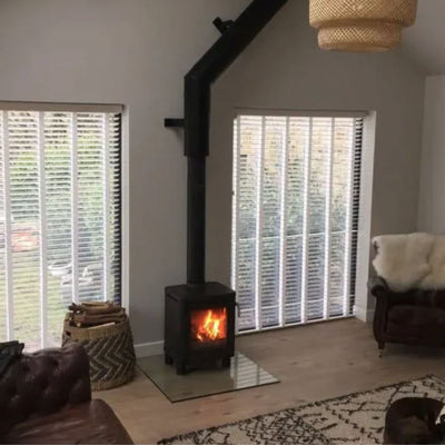 Lit woodburner with a twin wall chimney in a room with a rug and wooden floor