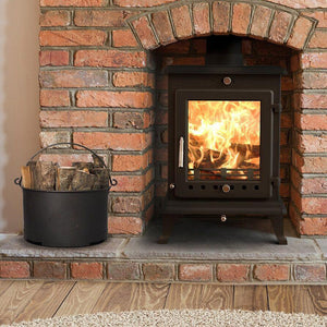 Cast iron wood burning stove in a brick recess with a brick hearth and metal bucket of logs