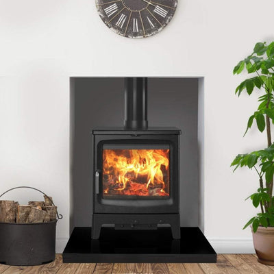 Saltfire Stoves Saltfire Peanut Bignut 5 Wood Burning Stove in a recess with a large clock above and on a thick black hearth