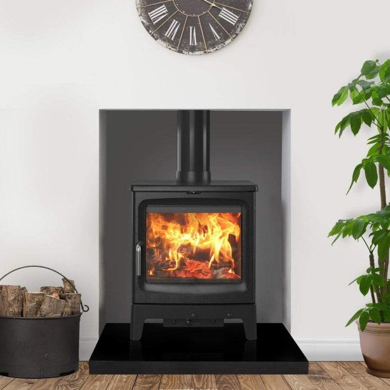 Saltfire Stoves Saltfire Peanut Bignut 5 Wood Burning Stove in a recess with a large clock above and on a thick black hearth