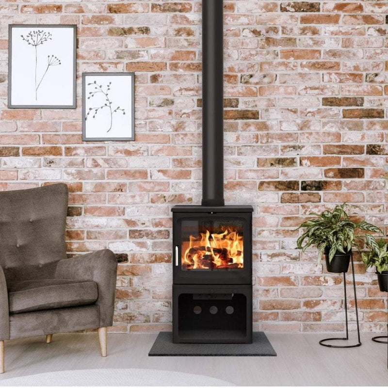 Saltfire Stoves Saltfire Peanut Bignut 5 Wood Burning Stove logstore version against a brick wall with a seat close by